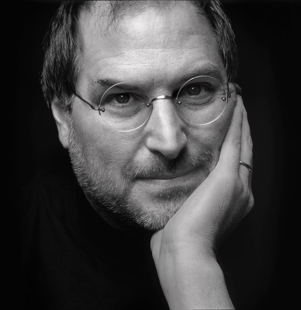 A black and white portrait of Steve looking directly into the camera, resting his chin in his hand.